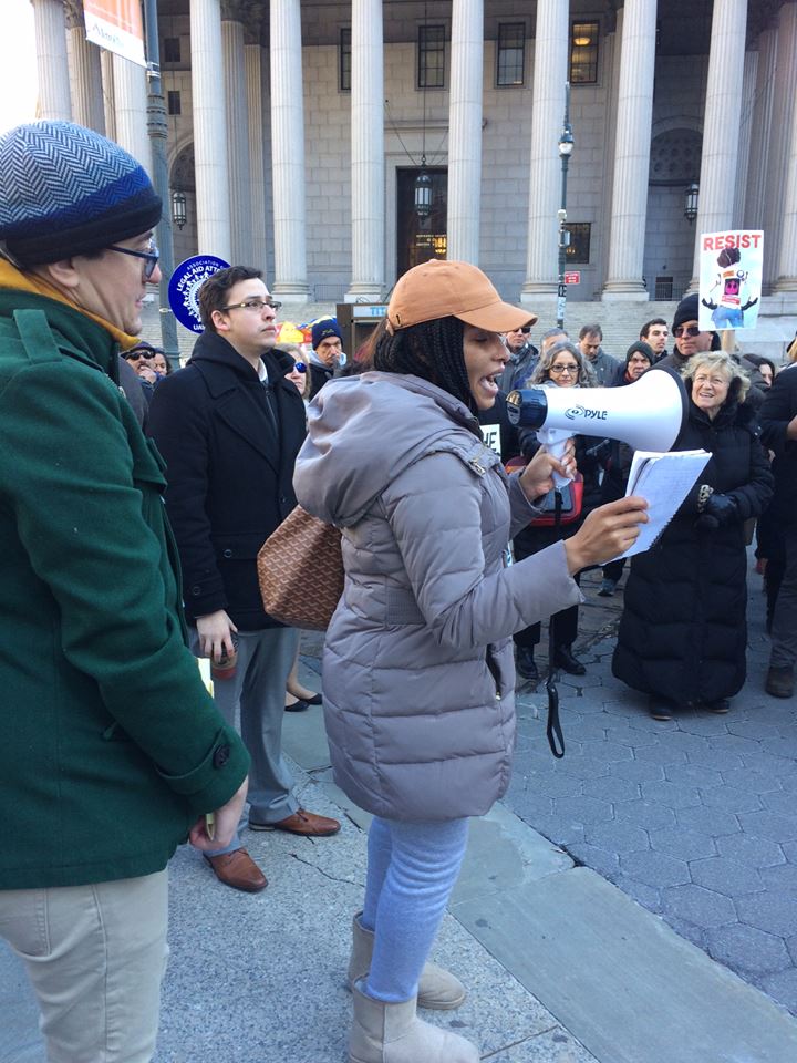 SRLP Movement Building Team member, Kimberly McKenzie, speaks out at the #LawStrikesBack rally. She is holding a megaphone is her hand and is standing in a crowd of protesters.