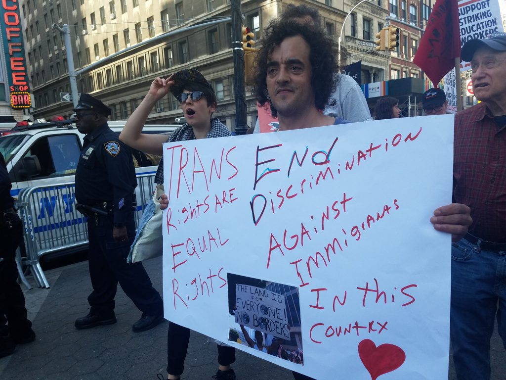 Movement Building Team member Stephanie at May Day rally holding up a sign taht reads "Trans Rights are Equal Rights. End Discrimination Against Immigrants in this Country".
